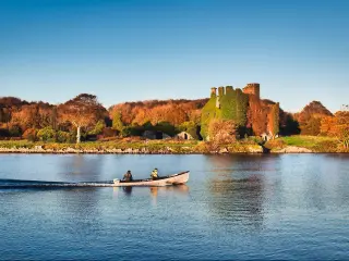 Beautiful scenery of Menlo castle surrounded by a autumn colored trees and boat passing by in Corrib river at Galway, Ireland