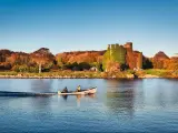 Beautiful scenery of Menlo castle surrounded by a autumn colored trees and boat passing by in Corrib river at Galway, Ireland