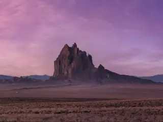 Wide, flat desert with large rock rising up, in pink light