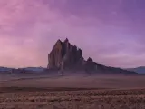 Wide, flat desert with large rock rising up, in pink light