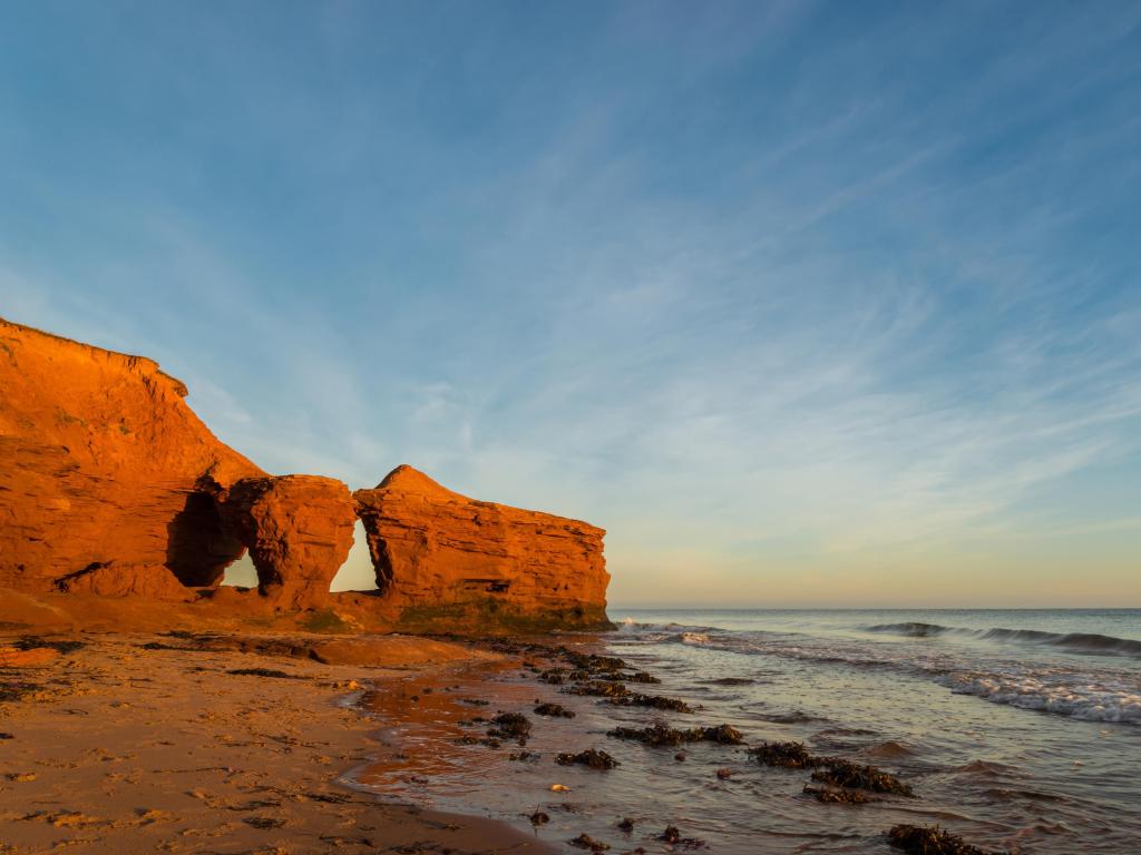 Green Gables Shore, Prince Edward Island, Canada with the red sandstone cliffs, beach and sea taken at sunset with a clear sky above.