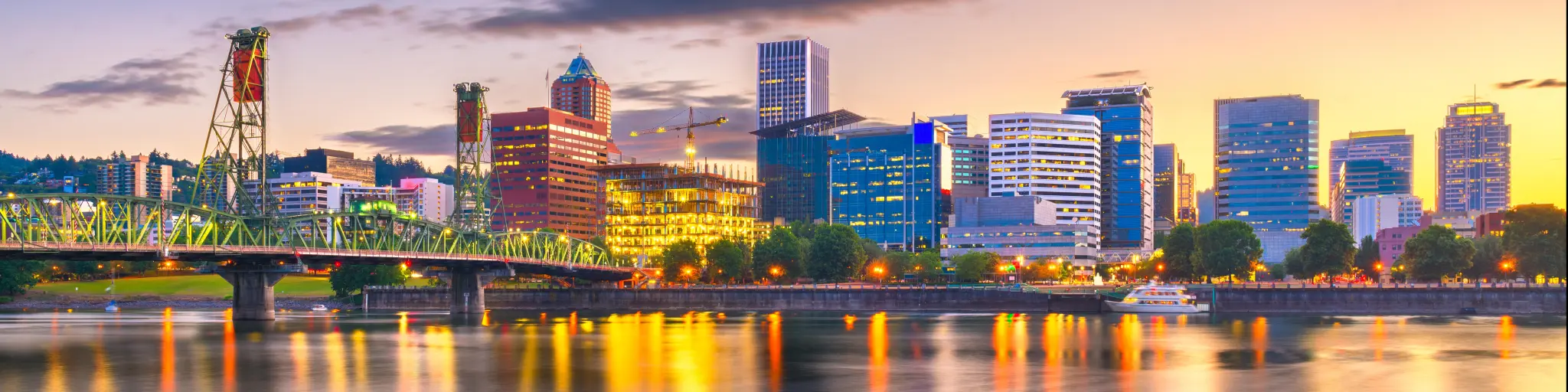 Portland, Oregon, USA with the skyline at dusk on the Willamette River, lights reflecting in the water and the bridge to the left of the photo.