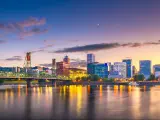 Portland, Oregon, USA with the skyline at dusk on the Willamette River, lights reflecting in the water and the bridge to the left of the photo.