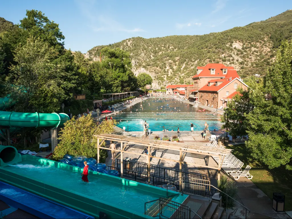 A wonderful sunny day at a public hot spring pool with water slide and a couple of people enjoying the hot water with a beautiful view of the mountain at Glenwood Springs, CA