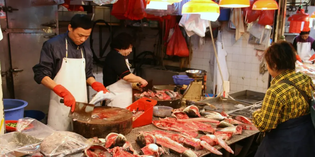 A man gutting a fish at a fish stall in a Hong Kong street market, with a woman cooking fish in the background
