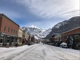 A street view in Telluride, Colorado where snow is on the road and some buildings are on the both sides of the road. The San Juan mountain can be seen on the background.t.