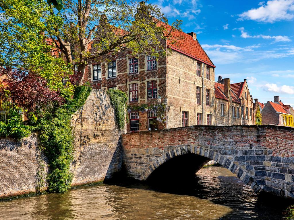 Bruges, Belgium with vintage stone houses and bridge over canal ancient medieval street picturesque landscape in summery sunny day with blue sky white clouds.