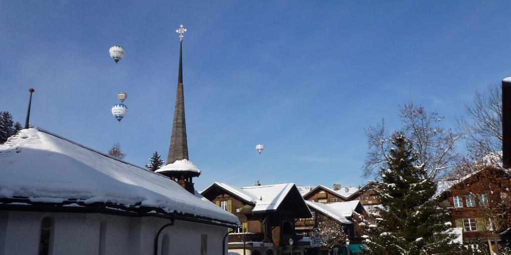 Hot air balloons taking off over the town of Gstaad, Switzerland, with a church spire in the foreground