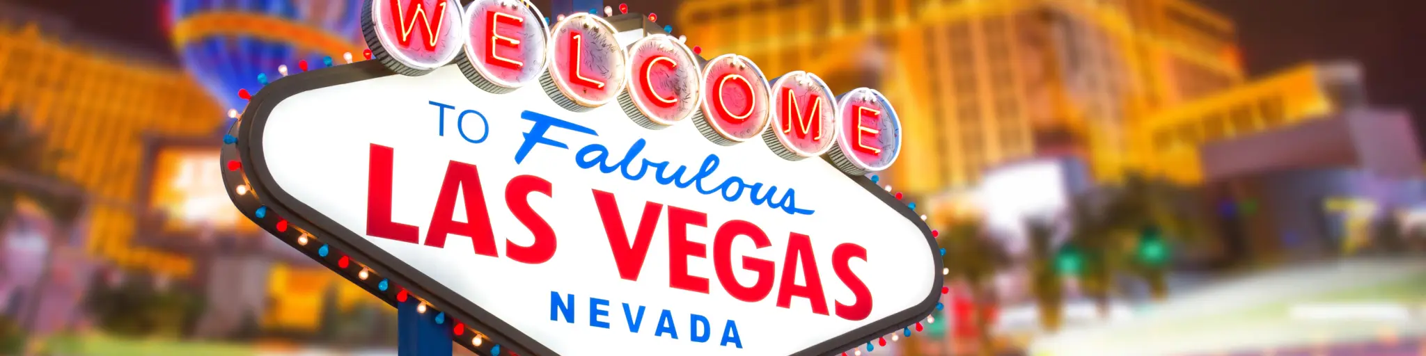 Neon-lit sign that reads "Welcome to Fabulous Las Vegas Nevada" with colorful lights of the hotels behind it