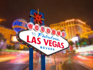 Neon-lit sign that reads "Welcome to Fabulous Las Vegas Nevada" with colorful lights of the hotels behind it