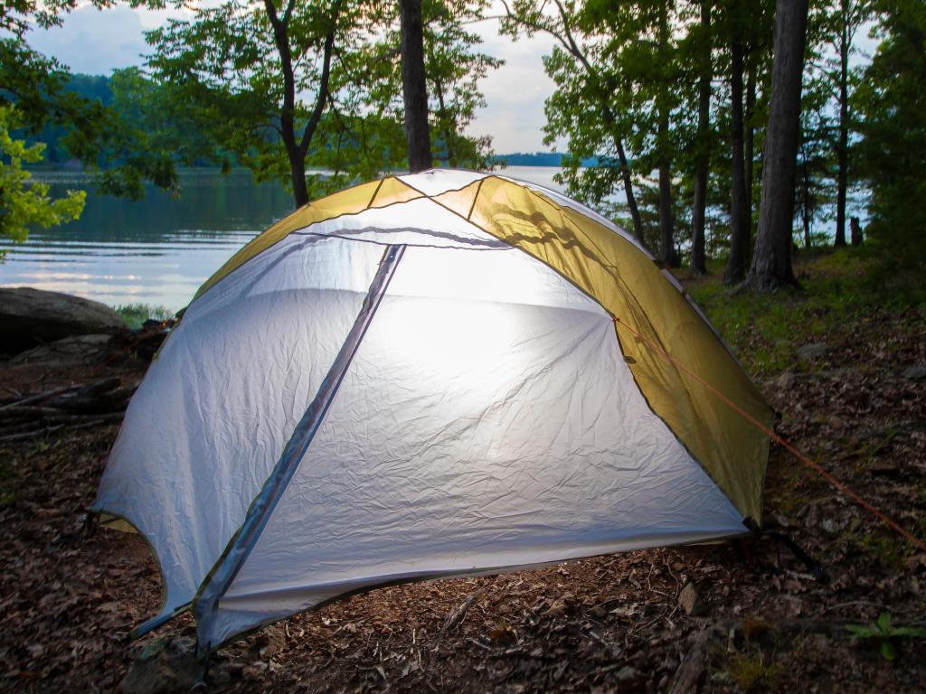 A tent set up in the forest next to Badin Lake, with light glowing from the inside