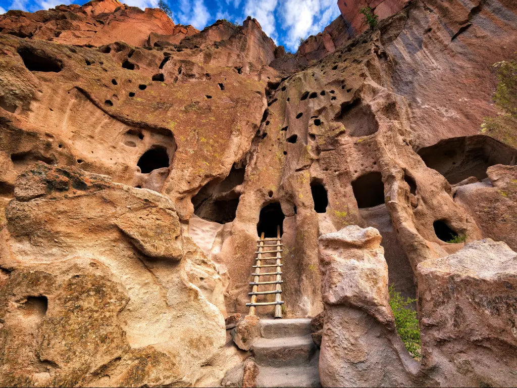 Bandelier National Monument, New Mexico, USA with cliff dwellings and a small wooden step ladder leading to a carved doorway, taken on a sunny day.