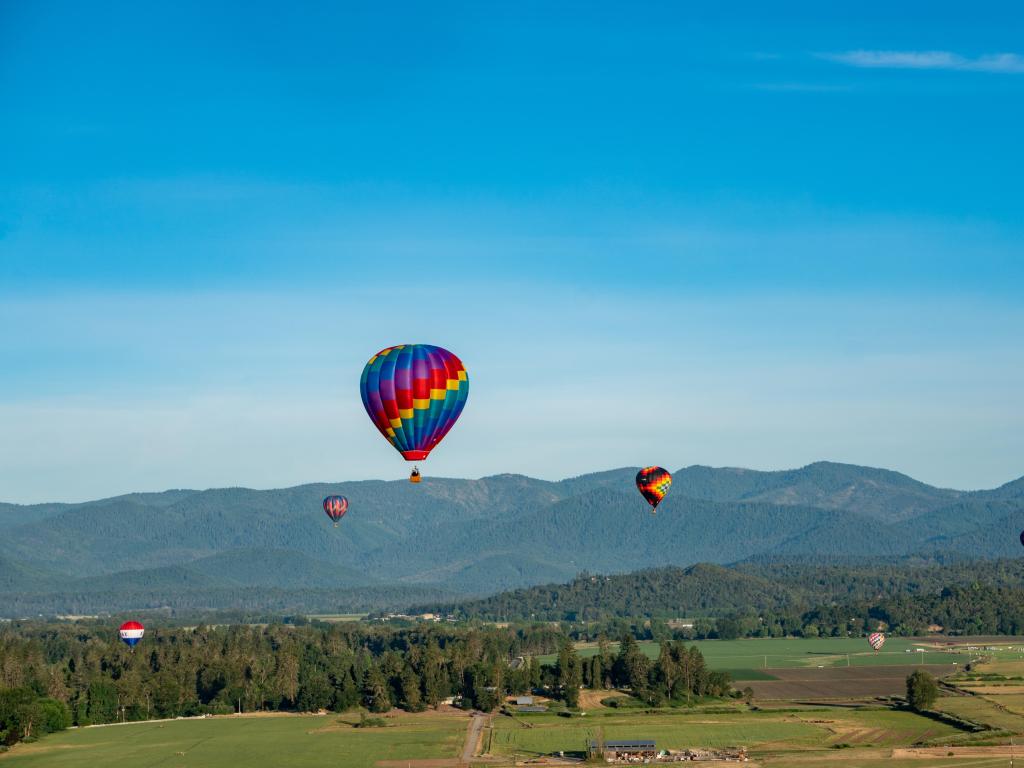 Grants Pass, Oregon, USA taken during the Balloon & Kite Festival with multi-colored balloons against a blue sky, hills in the distance.