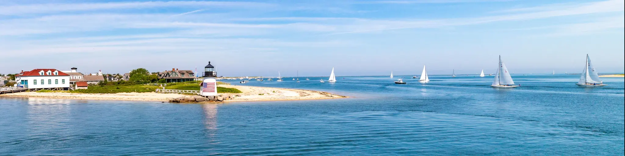 Lighthouse and sailboats under a blue sky day in the Nantucket Harbor.