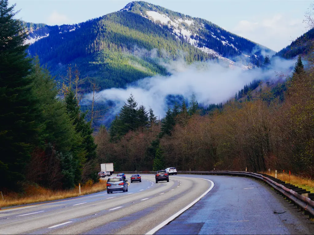 Early morning with cars driving along Snoqualmie Pass road passing tall green pine trees and taking in the breathtaking view of the mountain with a thin sheet of fog