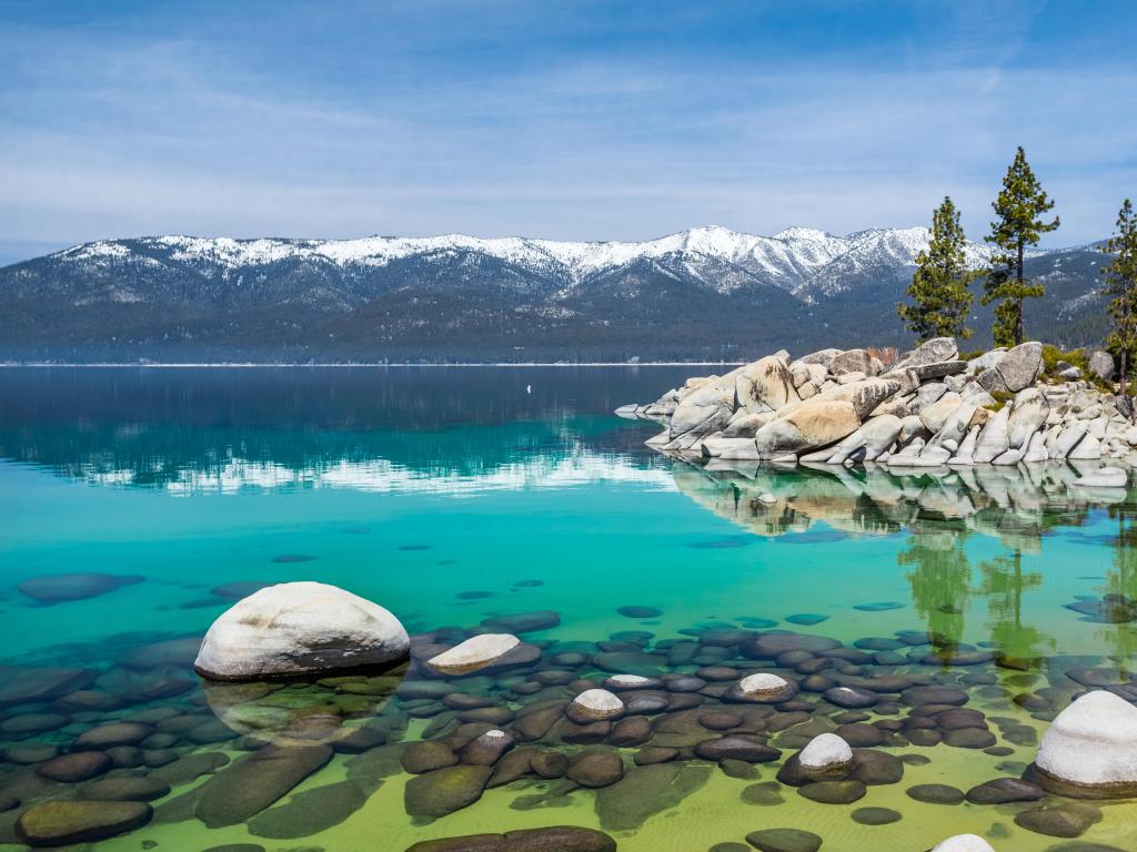 Lake Tahoe, USA taken at Sand Harbor Beach with a turquoise sea and large rocks in the water, with snow-capped mountains in the background and a blue sky.