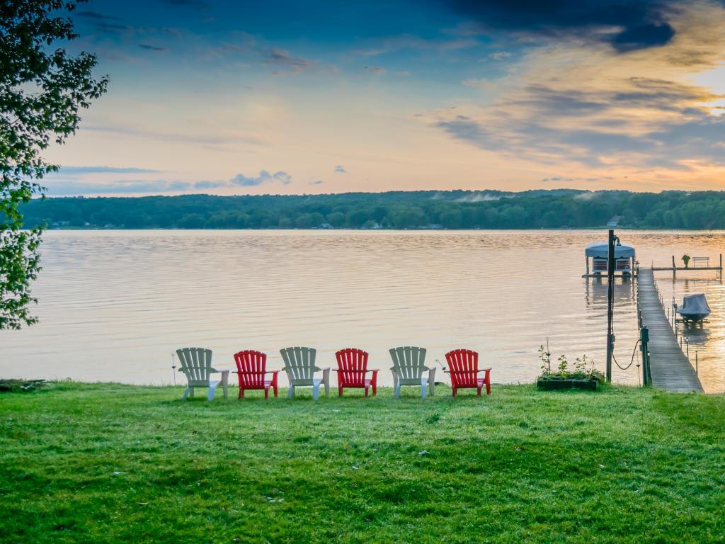 Line of red and white chairs overlooking the calm waters and sun setting at Lake Chautauqua in Western New York State