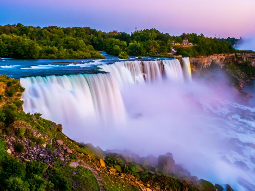 Niagara falls in the summer during beautiful evening, night with clear dark sunset blue sky. Niagara fall water hit with many colorful lights that is beautiful in a way. Sky turning dark and cold.