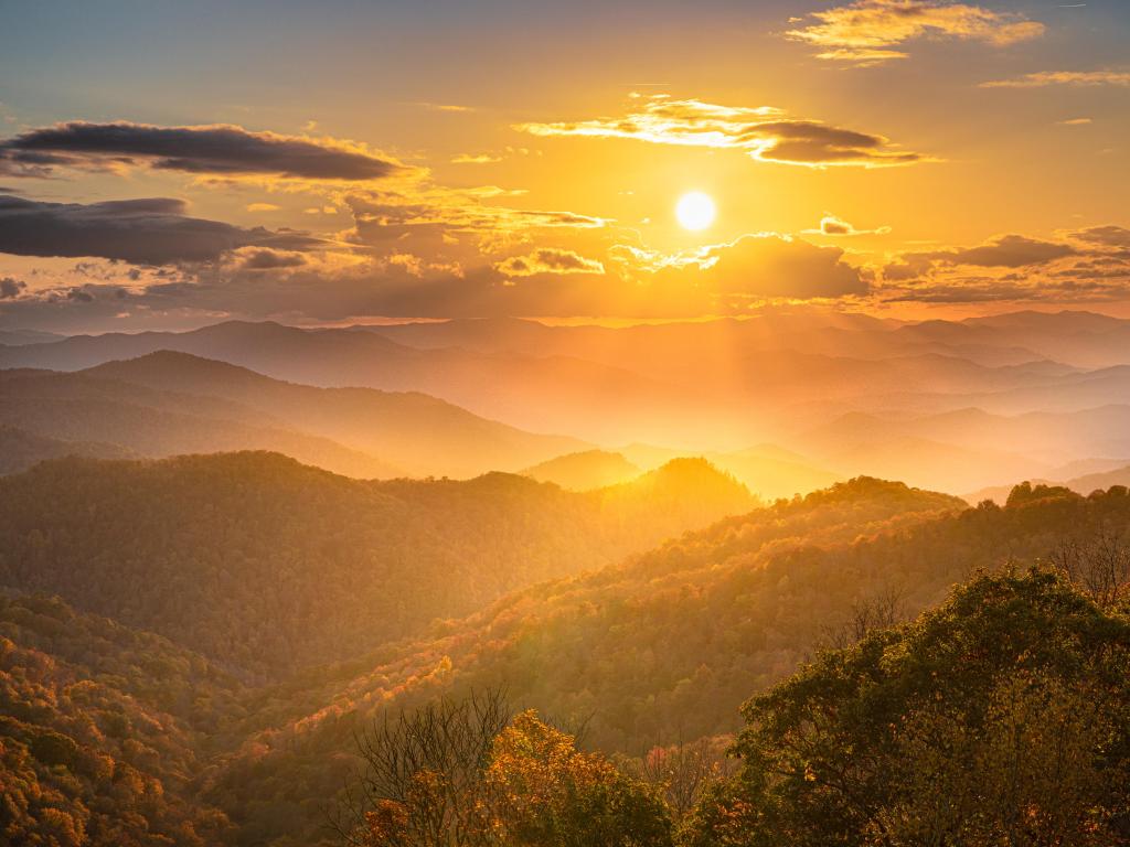 Bright orange sunset illuminating mountain slopes covered in trees