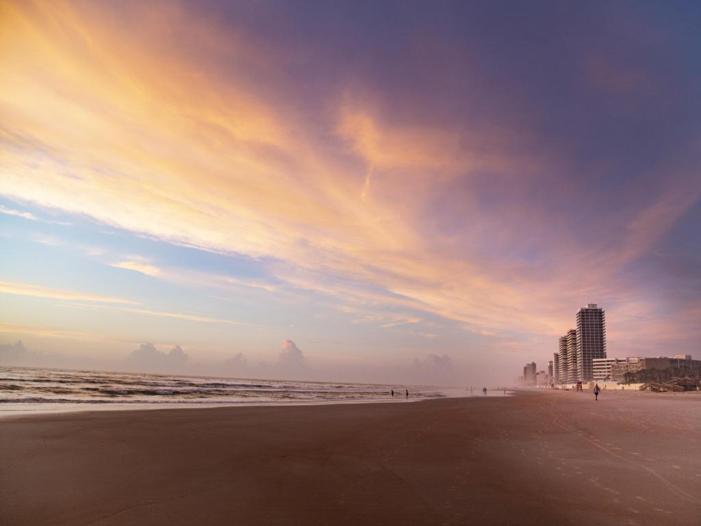 Daytona Beach, Florida, USA with a breathtaking view of a pink sunset and a view of the beach with buildings in the distance.