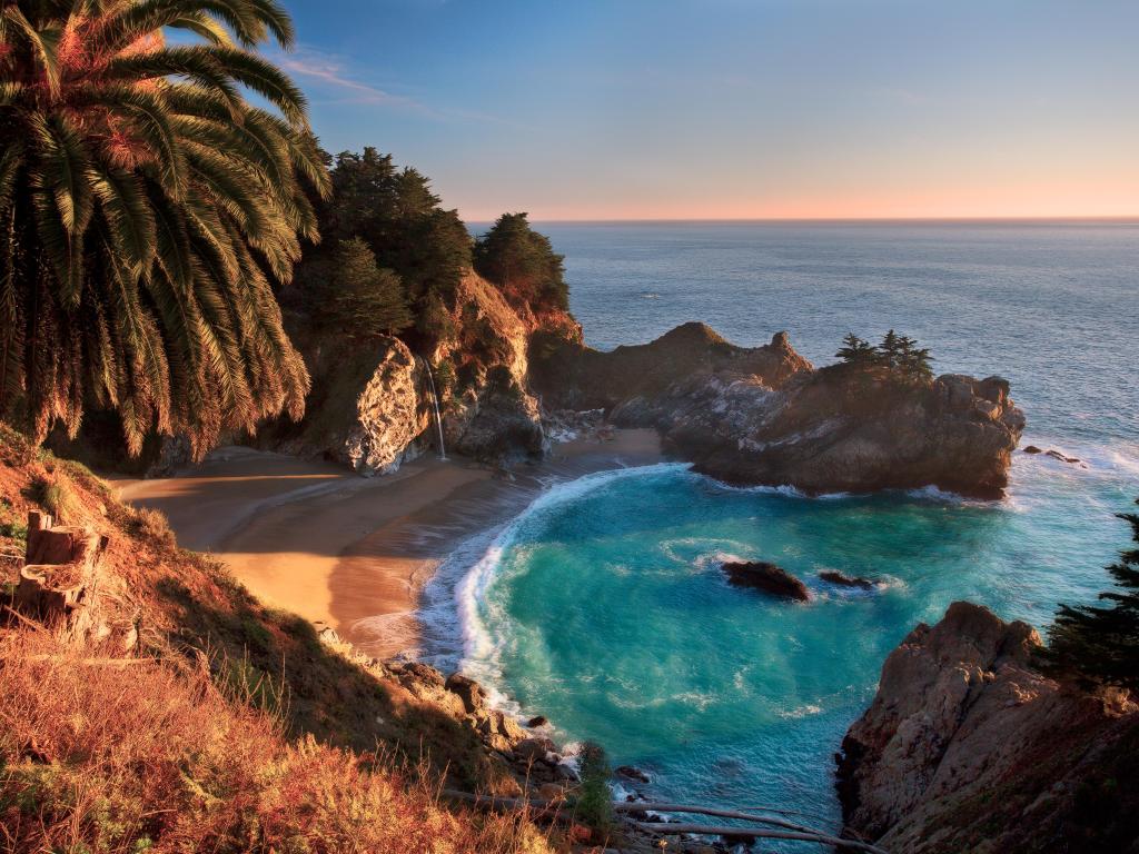 Sunset view of McWay Falls at Big Sur, with the sea lapping at the bay