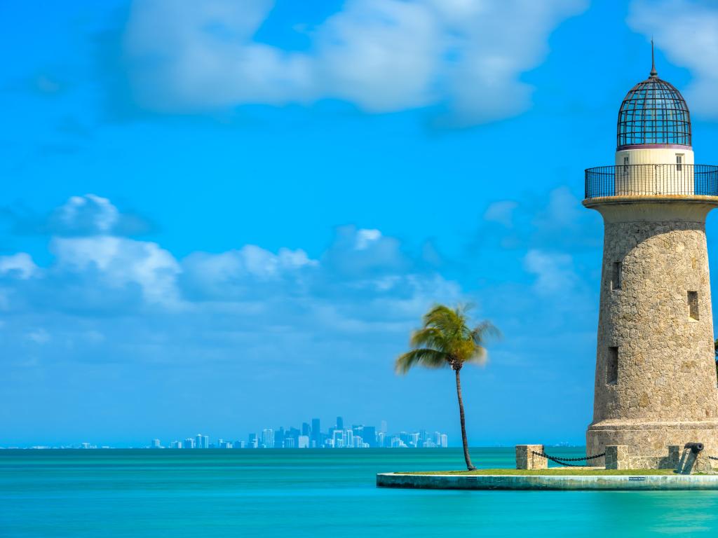 Biscayne National Park with Boca Chita Lighthouse in the foreground surrounded by turquoise sea and Miami skyline in the distance on a calm day.