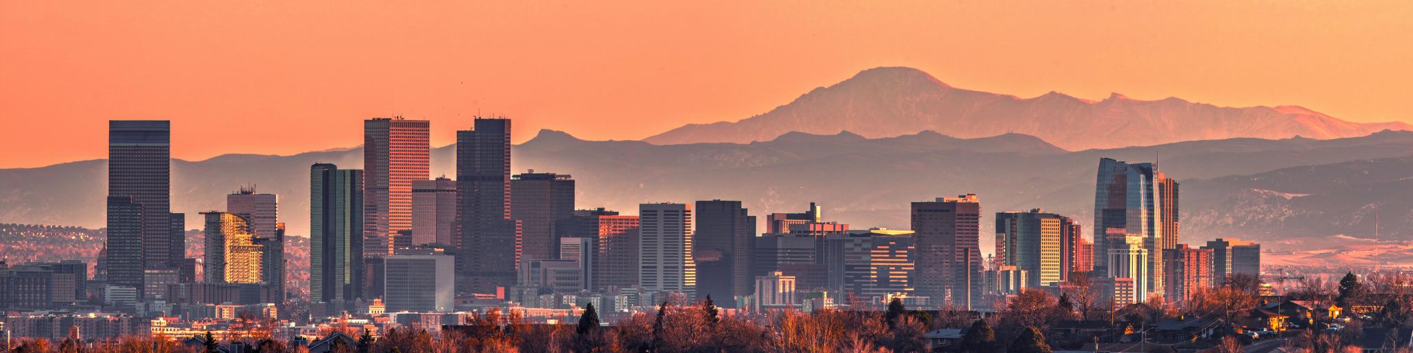 Denver skyline at sunset with Rocky Mountains in the background.