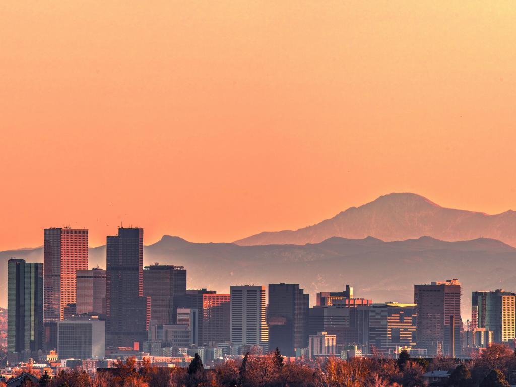 Denver skyline at sunset with Rocky Mountains in the background.