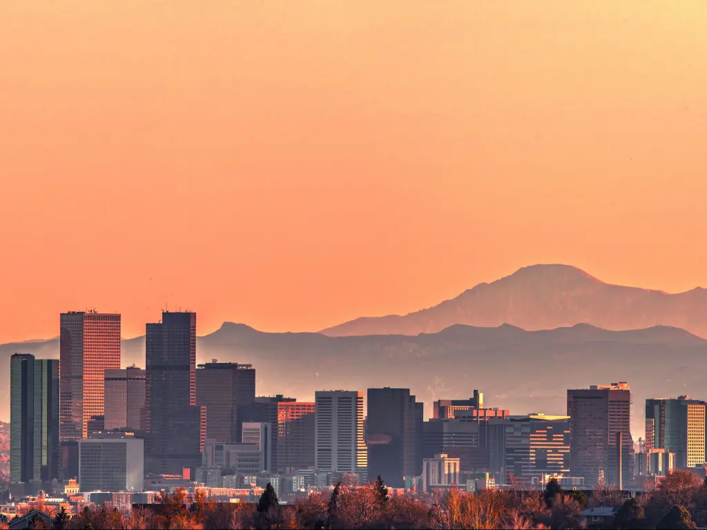 Denver skyline at sunset with Rocky Mountains in the background.