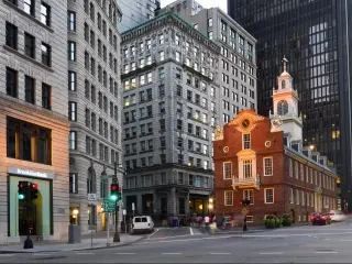 Historic low rise brick built building surrounded by grey sky scrapers