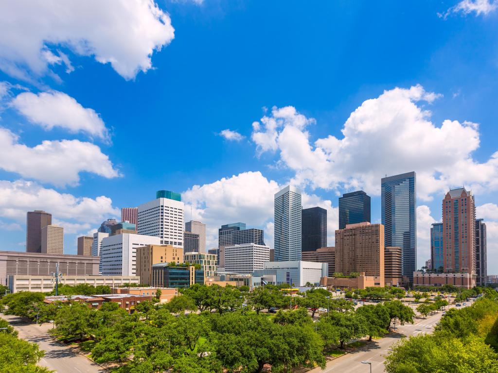 Houston, Texas, USA skyline with trees in the foreground against a cloudy blue sky. 