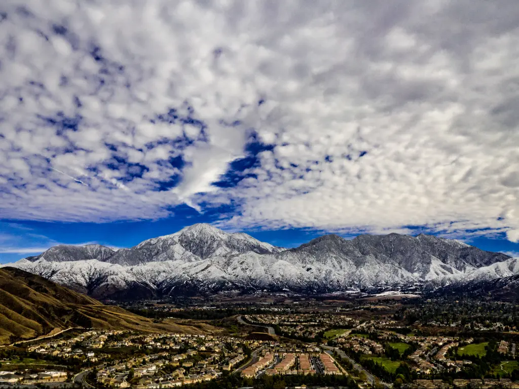A stunning aerial view of San Gorgonio and Little San Bernardino Mountains covered in snow on a winter day with blue mackerel skies of white and grey clouds.