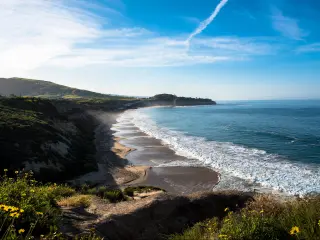 Dana Point, California, USA with coast views and the beach, green cliffs in the distance on a sunny day.