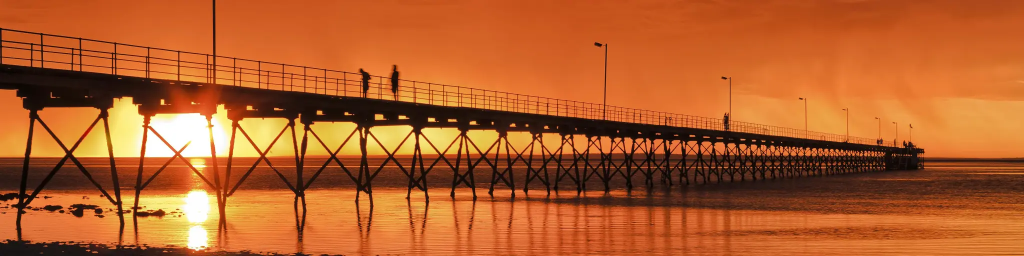 Low point view of wooden historic jetty in Ceduna with an incredibly dramatic orange sunset