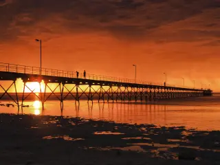 Low point view of wooden historic jetty in Ceduna with an incredibly dramatic orange sunset
