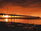 Low point view of wooden historic jetty in Ceduna with an incredibly dramatic orange sunset