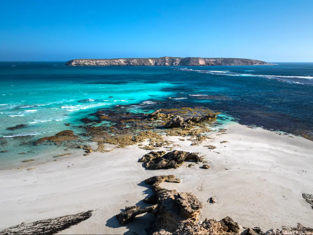 Coffin Bay National Park, Eyre Peninsula, South Australia with rocks and white sand in the foreground, a blue sea and island in the distance on a clear day.