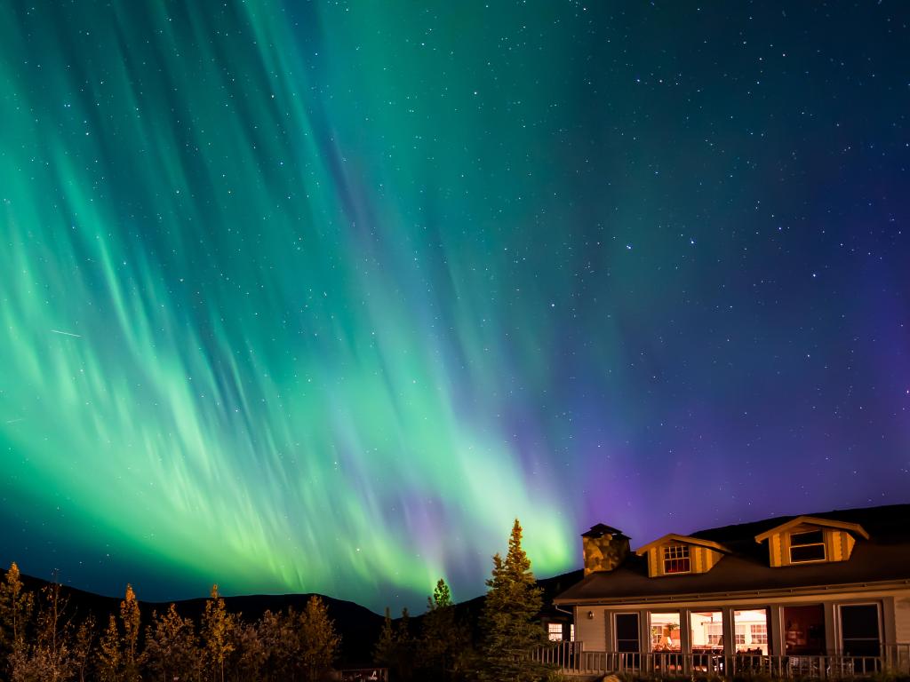 Lodge located near Mount Denali, green Northern lights scattering in the night sky 