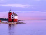 The historic Round Island Lighthouse at the shore of Mackinac Island in a purple and blue sky after sunset with a view of green pine trees at the distance