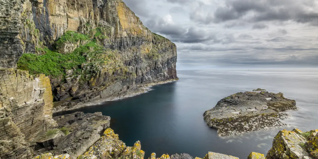 The grey cliffs and dark waters of the cove surrounding the harbour that the Whaligoe Steps lead to, in Scotland