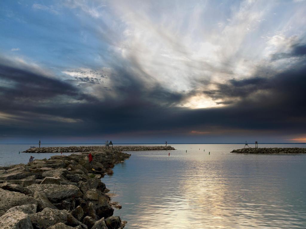 Lake Winnebago, USA with a sunset on the waters, rocks in the distance leading out towards the lake and a moody sky above.
