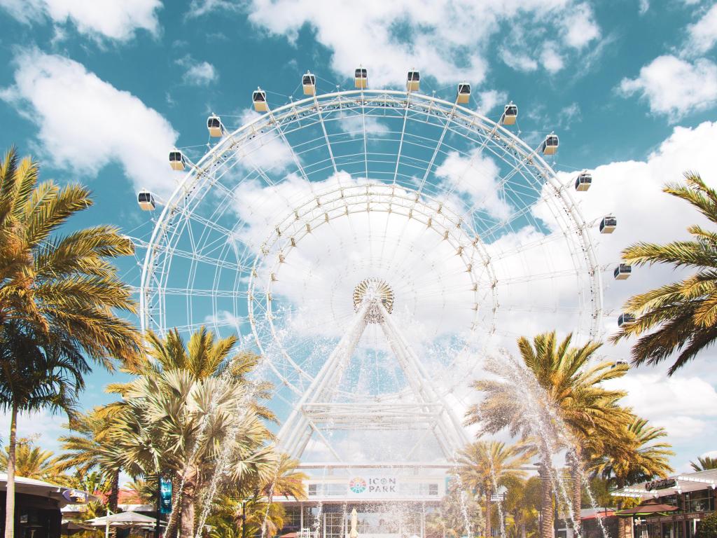 Orlando, Florida, USA with a view of the Orlando Eye against a cloudy but sunny sky and palm trees in the foreground. 