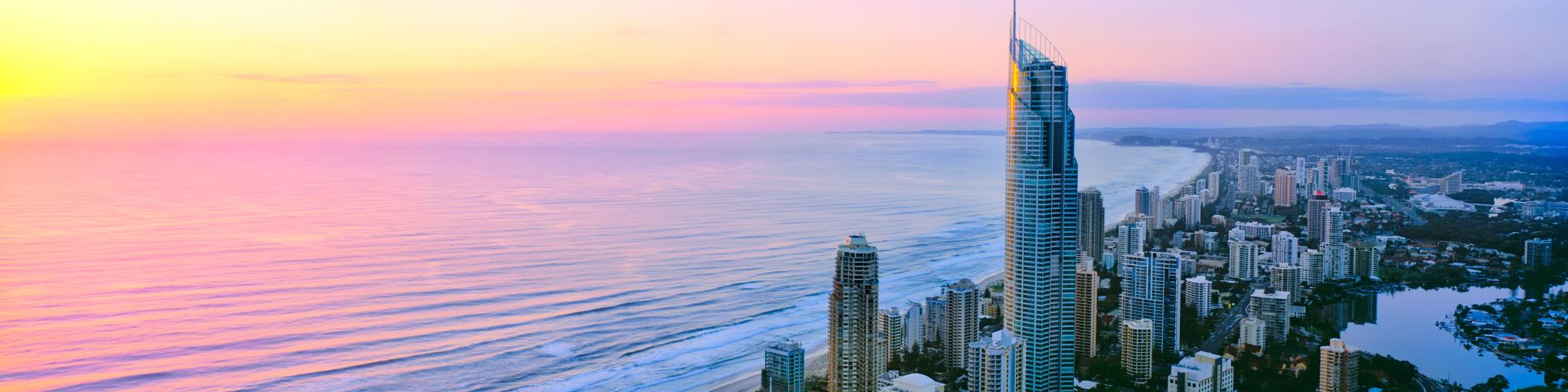 Sunrise casts a pink light over a long stretch of coast with highrise buildings
